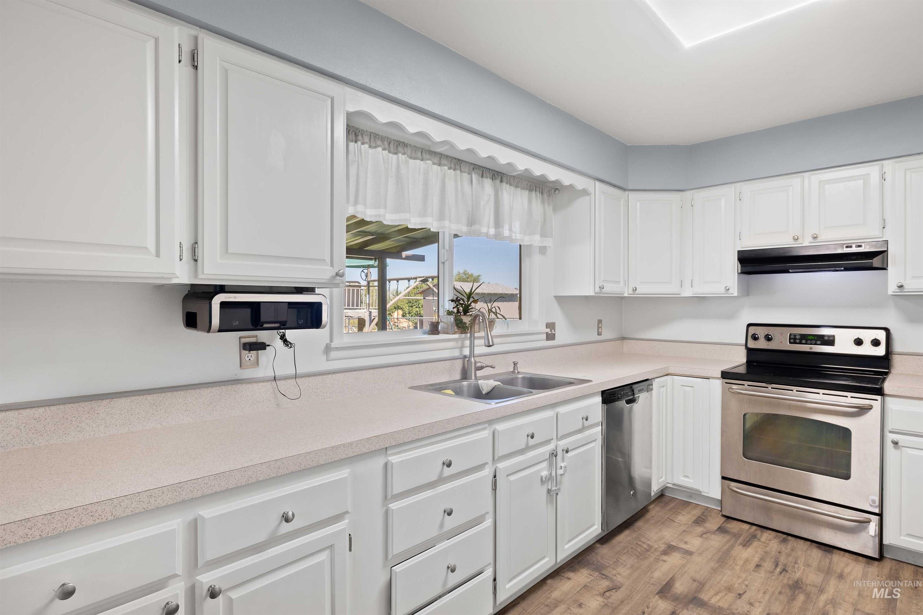 Kitchen with appliances with stainless steel finishes, light wood-style floors, white cabinets, and light countertops