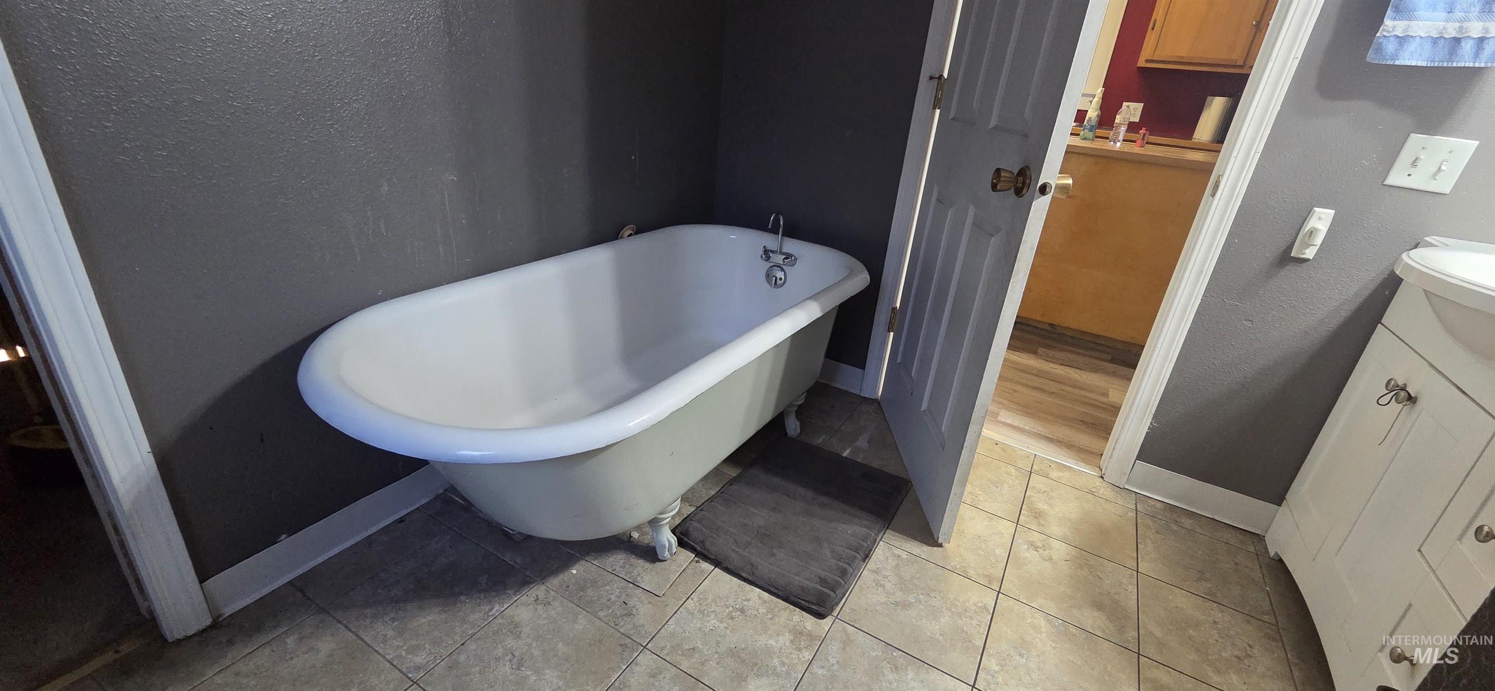 Bathroom featuring a freestanding tub, vanity, a textured wall, and light tile patterned floors