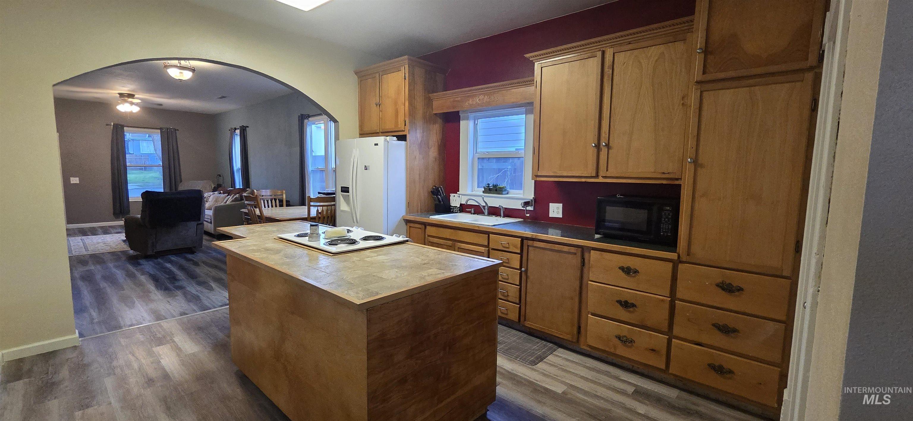 Kitchen with arched walkways, white appliances, dark wood-style floors, a center island, and wood finish cabinetry