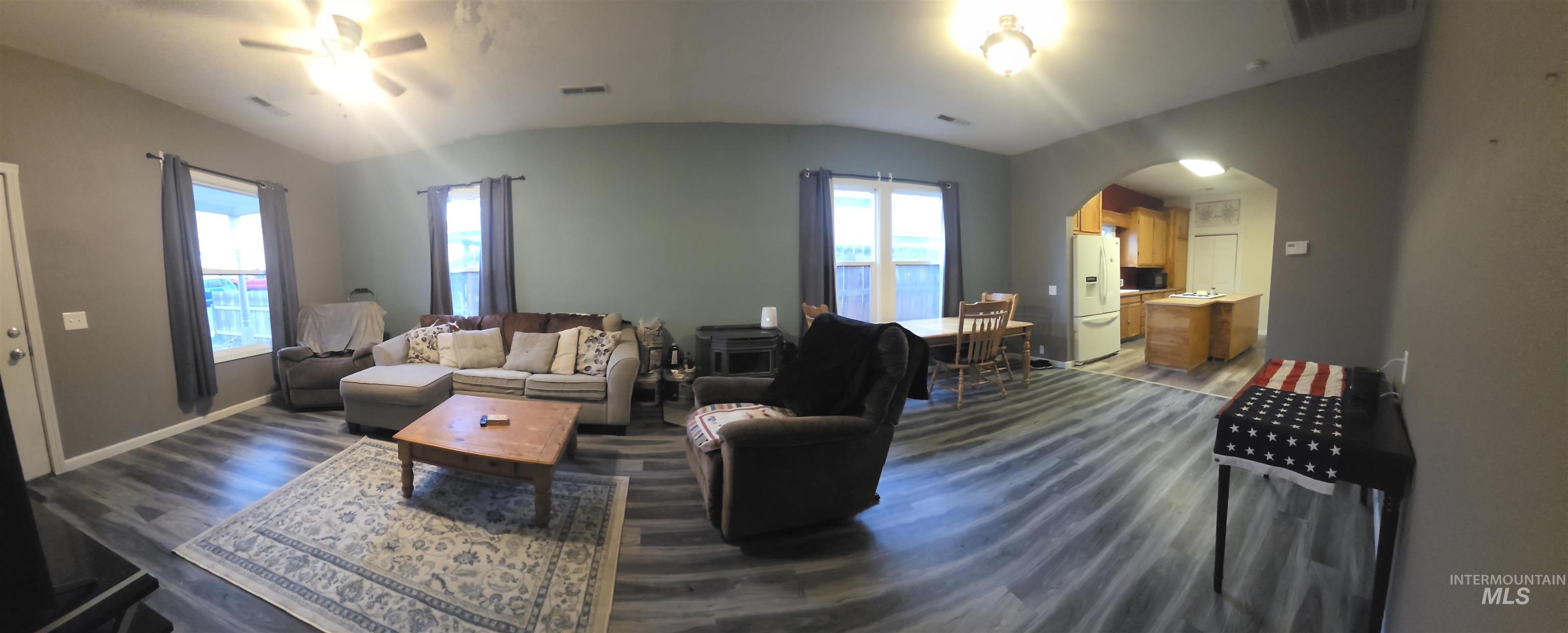 Living area with ceiling fan, dark wood finished floors, lofted ceiling, arched walkways, and plenty of natural light