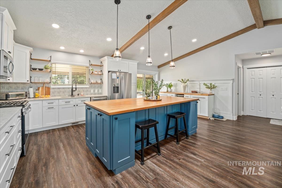 Kitchen featuring appliances with stainless steel finishes, open shelves, butcher block countertops, blue cabinetry, and white cabinetry