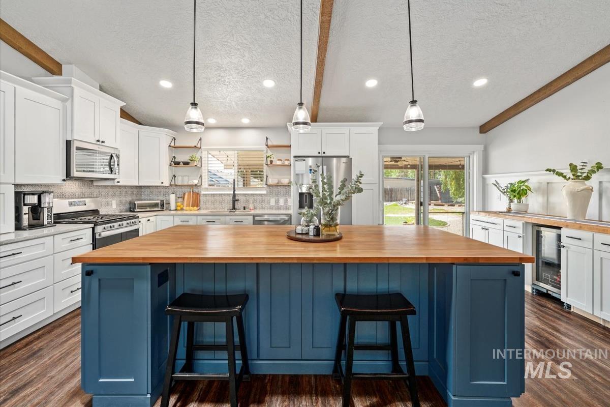 Kitchen with butcher block counters, open shelves, stainless steel appliances, beverage cooler, and plenty of natural light