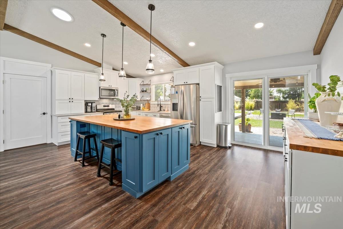 Kitchen with butcher block countertops, appliances with stainless steel finishes, blue cabinetry, open shelves, and white cabinets