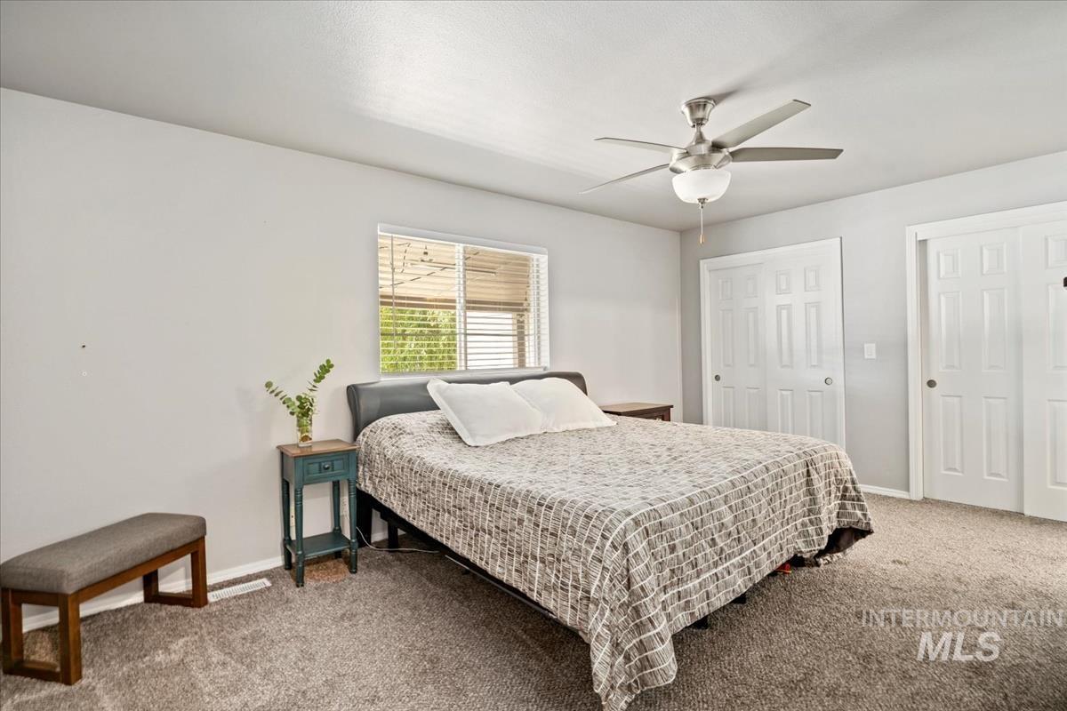 Bedroom featuring light carpet, multiple closets, and a ceiling fan