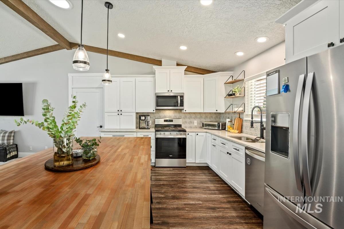 Kitchen featuring appliances with stainless steel finishes, wood counters, open shelves, decorative backsplash, and hanging light fixtures