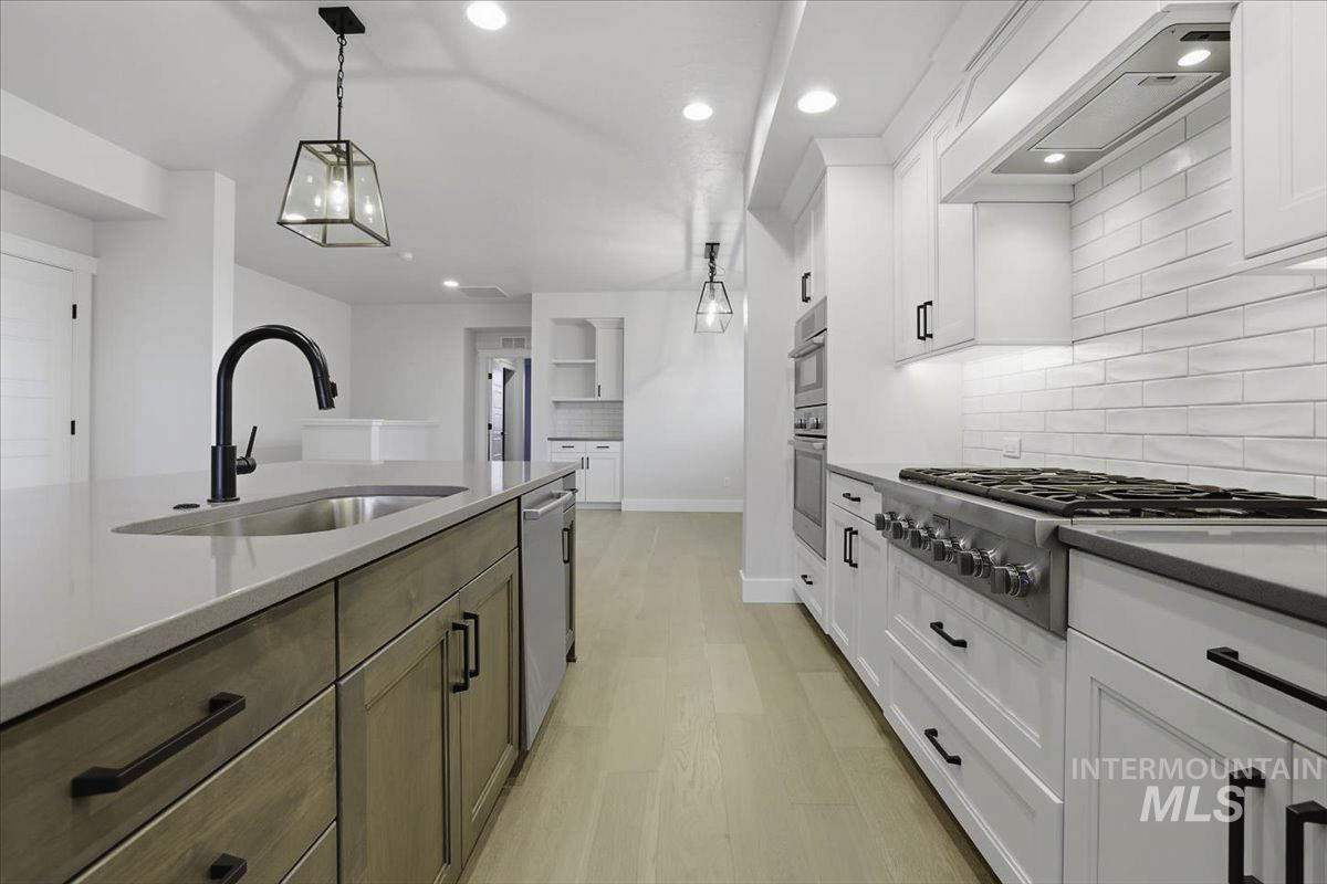 Two tone kitchen with stainless steel appliances, two tone cabinetry, light stone counters, light wood-style floors, and backsplash