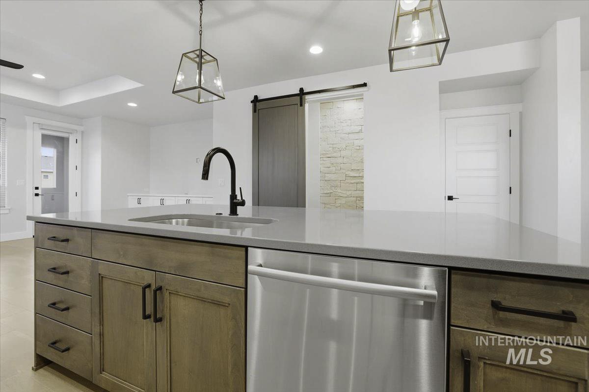 Kitchen with stainless steel dishwasher, a barn door, light stone counters, and decorative light fixtures
