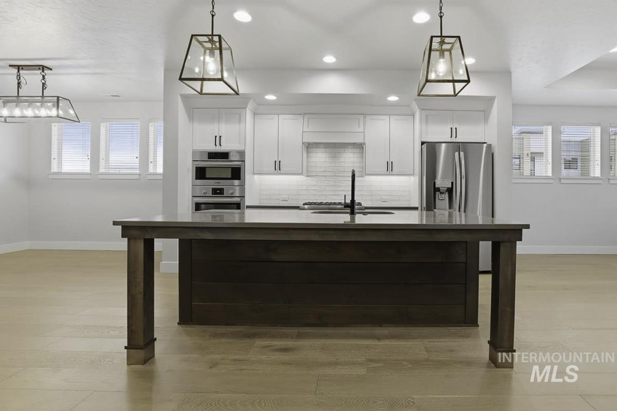 Kitchen with light wood-style flooring, an island with sink, white cabinets, and hanging light fixtures