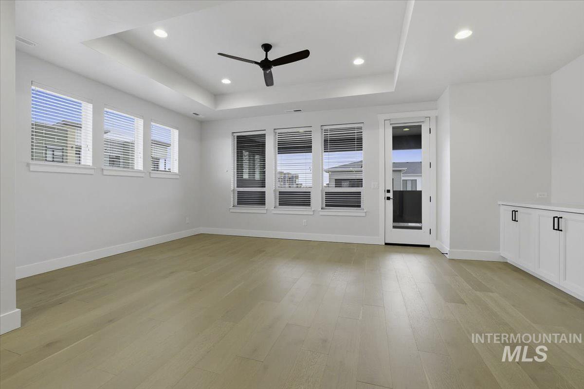 Unfurnished room with a ceiling fan, healthy amount of natural light, light wood-style flooring, recessed lighting, and a raised ceiling
