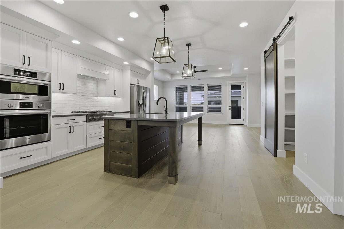 Kitchen with a breakfast bar area, stainless steel appliances, decorative backsplash, a barn door, and two tone color scheme