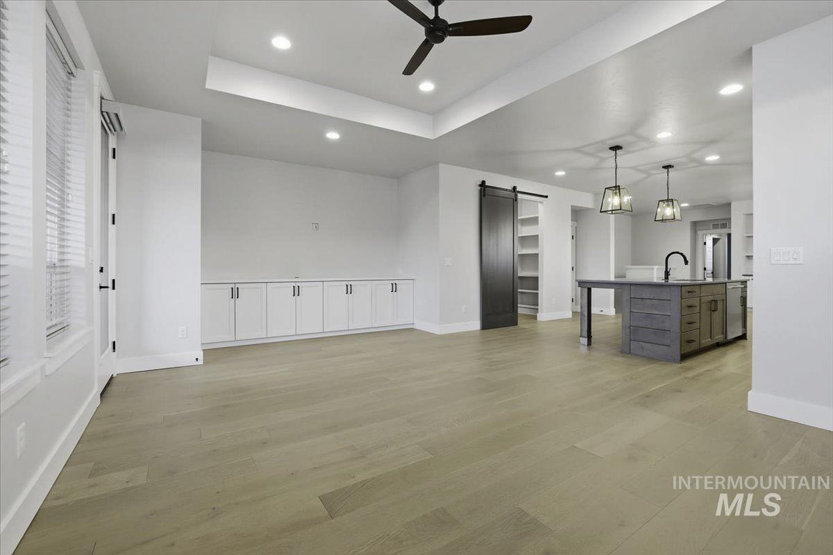 Kitchen featuring a barn door, a breakfast bar area, a kitchen island with sink, ceiling fan, and light wood-style flooring