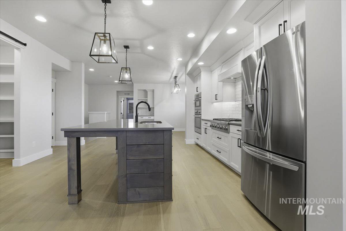 Kitchen with stainless steel appliances, decorative backsplash, white cabinetry, an island with sink, and light wood-style floors
