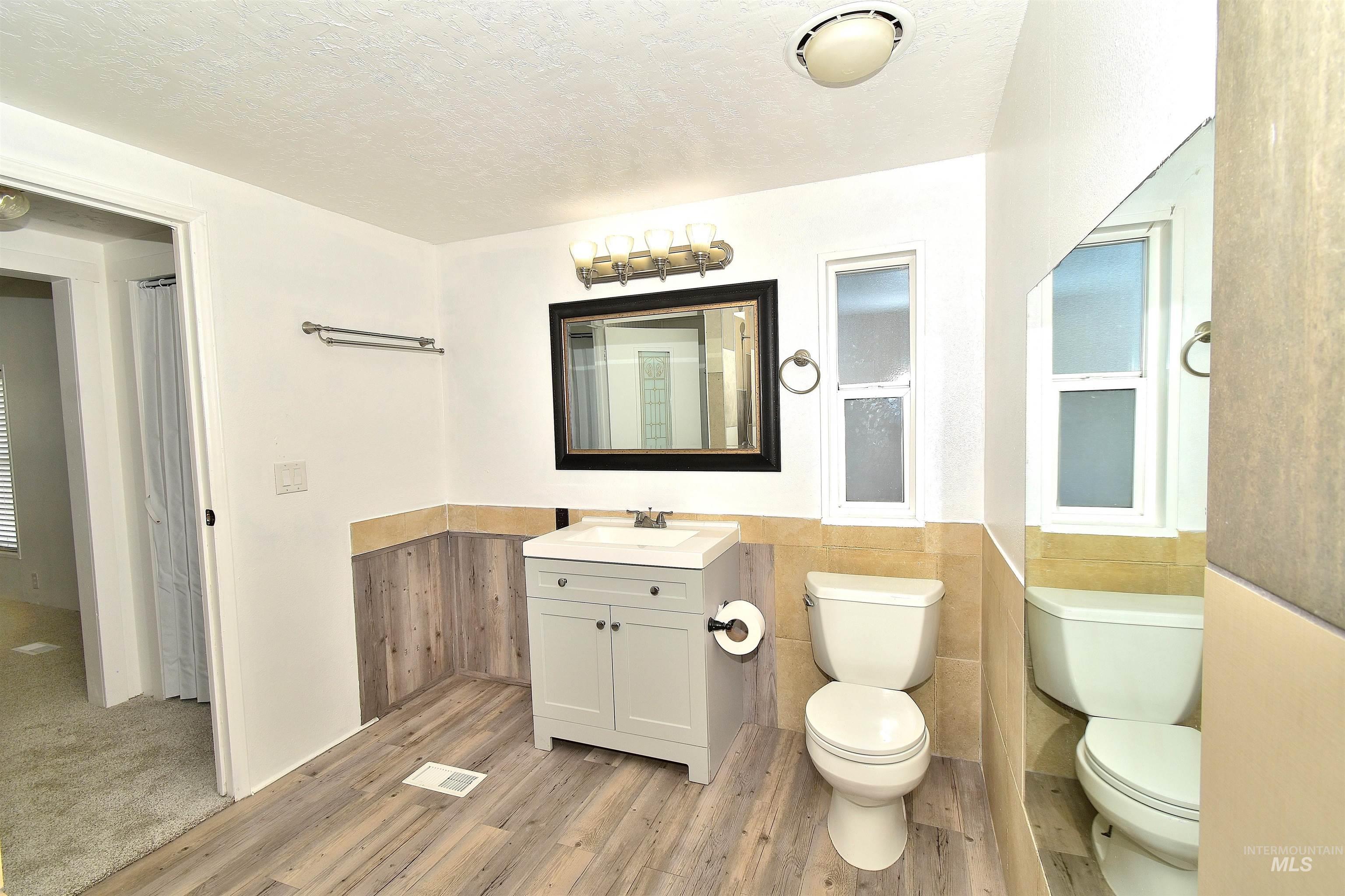Bathroom featuring vanity, a textured ceiling, light wood-style floors, and wainscoting