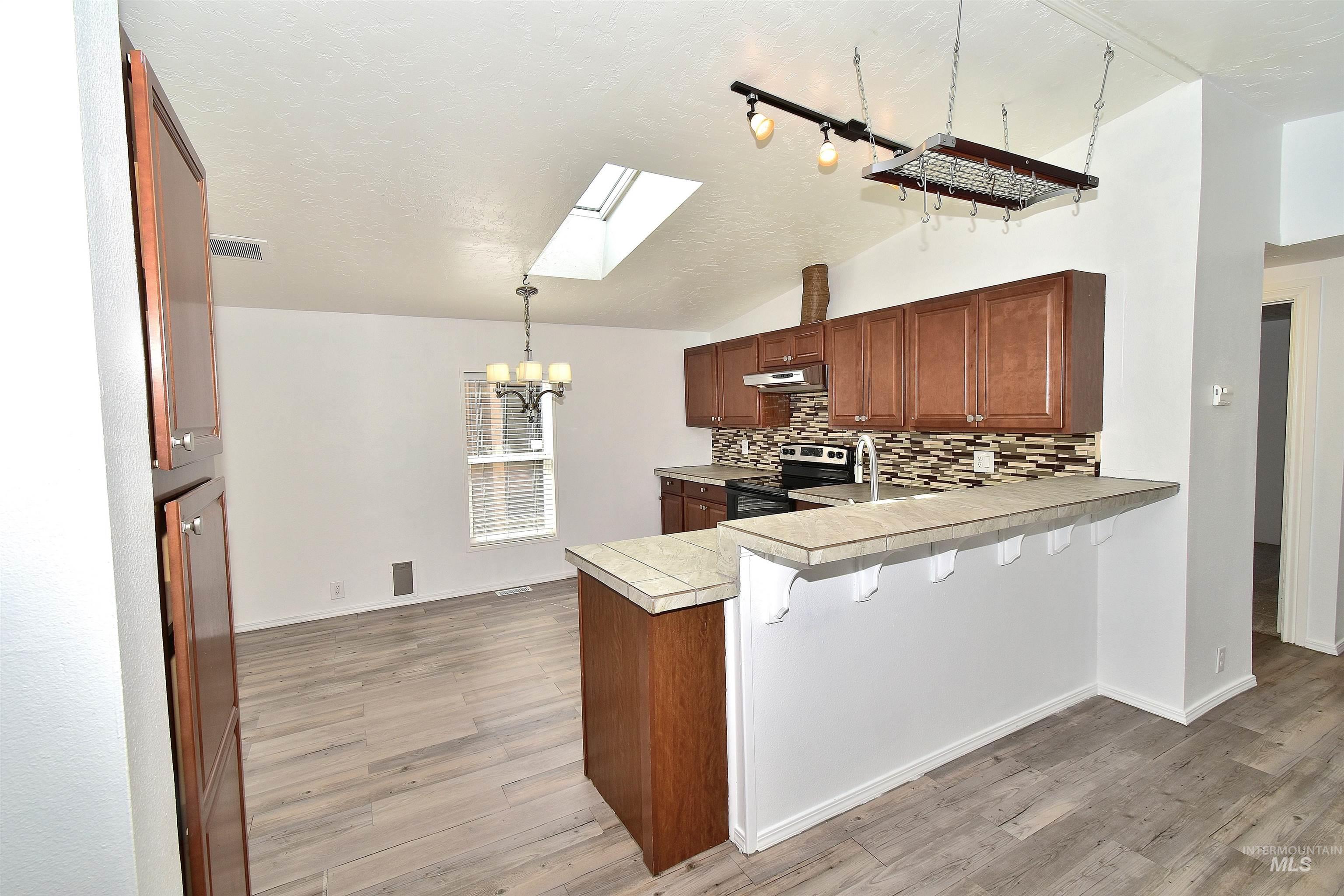 Kitchen with a skylight, hanging lights, decorative backsplash, a breakfast bar, and stainless steel range with electric stovetop