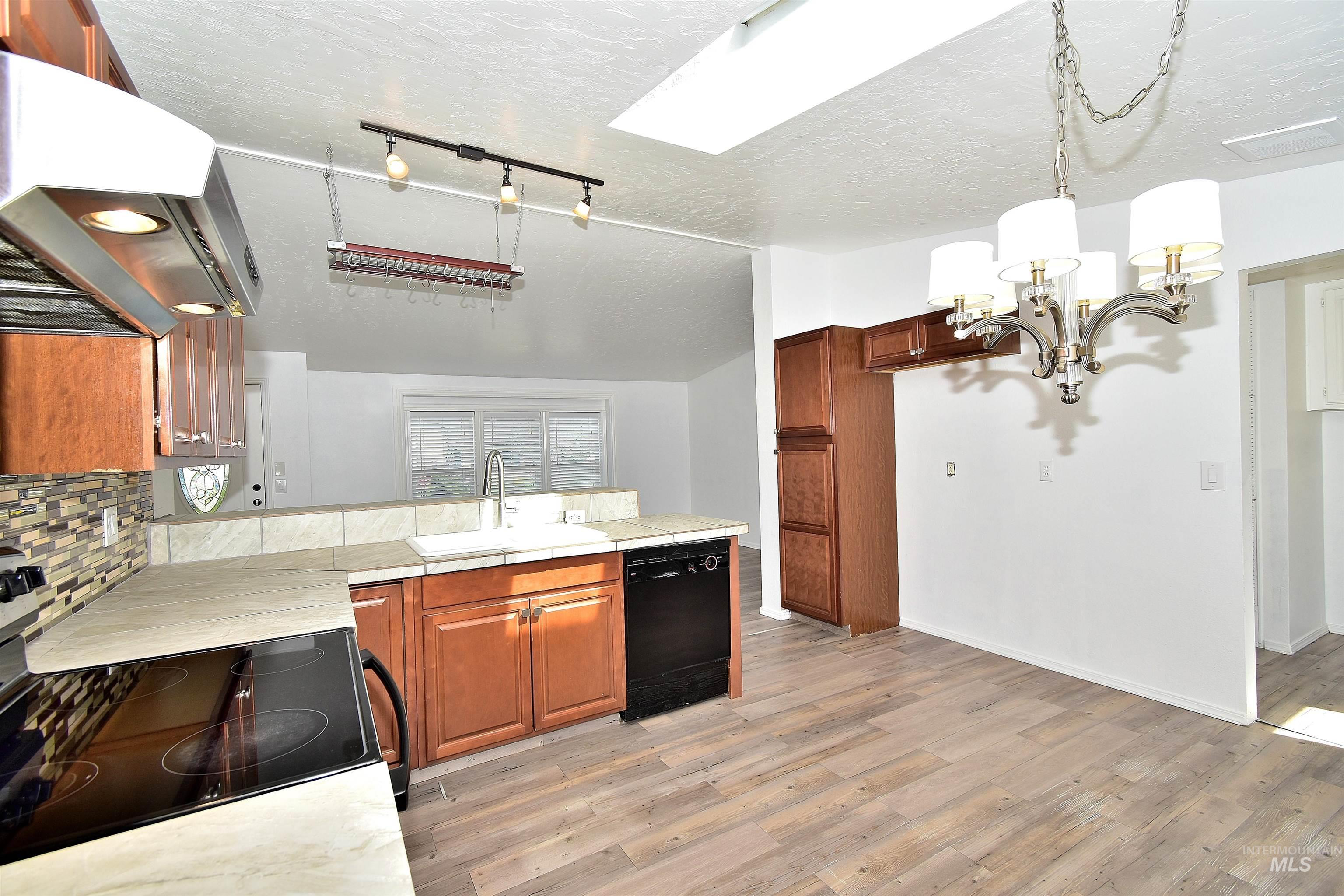Kitchen with light countertops, electric stove, wood finish cabinetry, black dishwasher, and suspended lighting