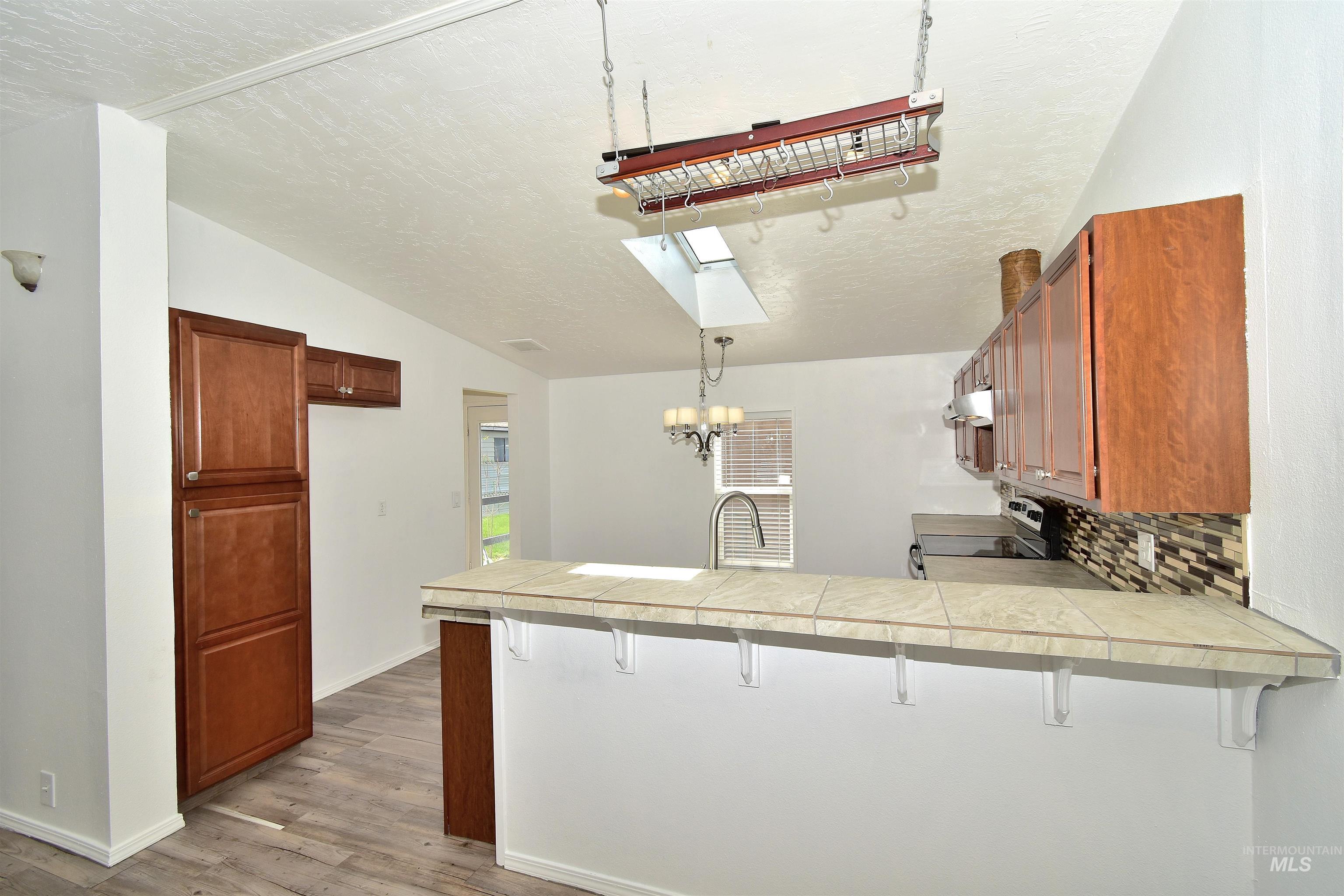 Kitchen featuring a kitchen breakfast bar, backsplash, stainless steel range with electric stovetop, wood finish cabinetry, and hanging lights