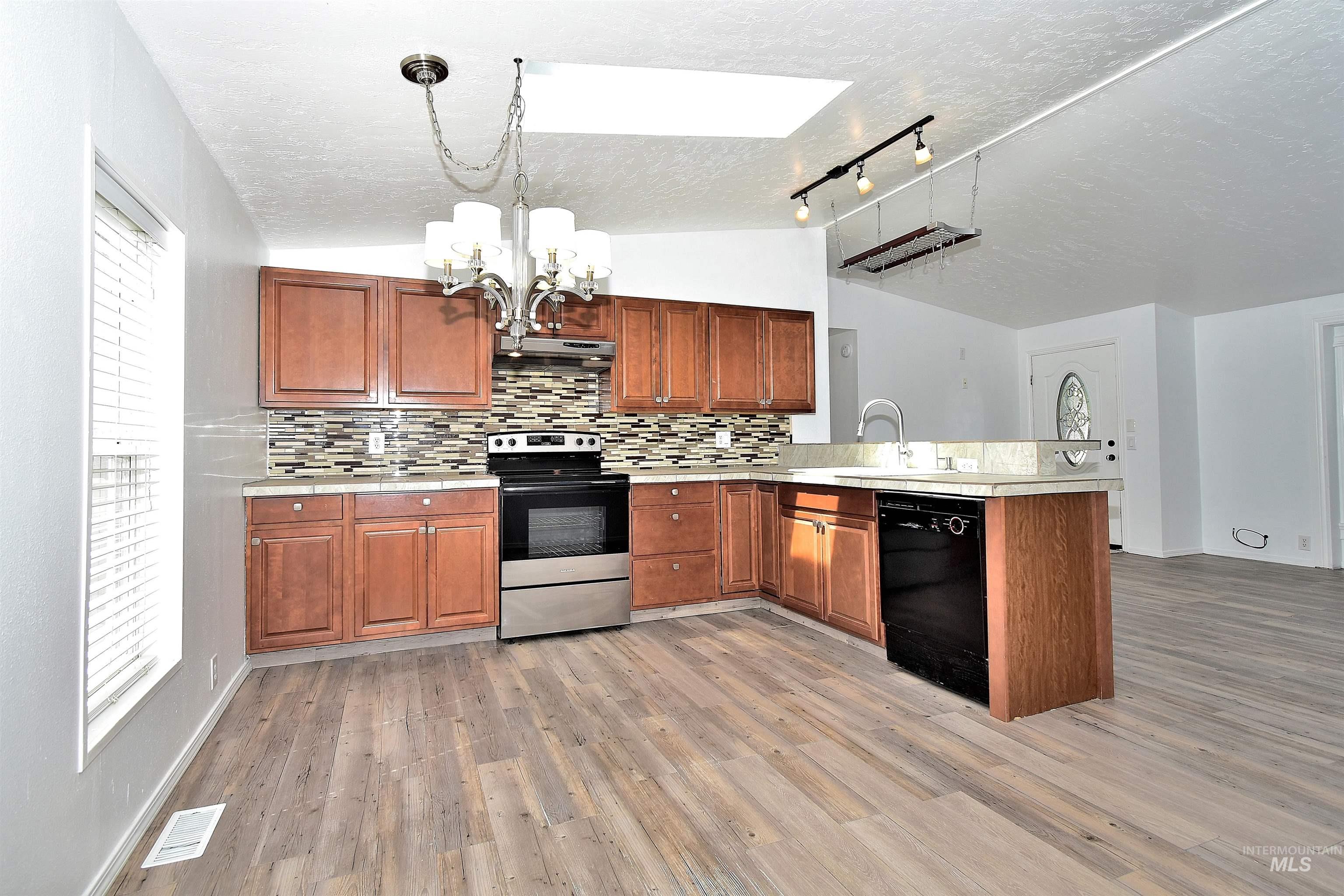 Kitchen featuring light countertops, stainless steel electric stove, tasteful backsplash, a peninsula, and a chandelier