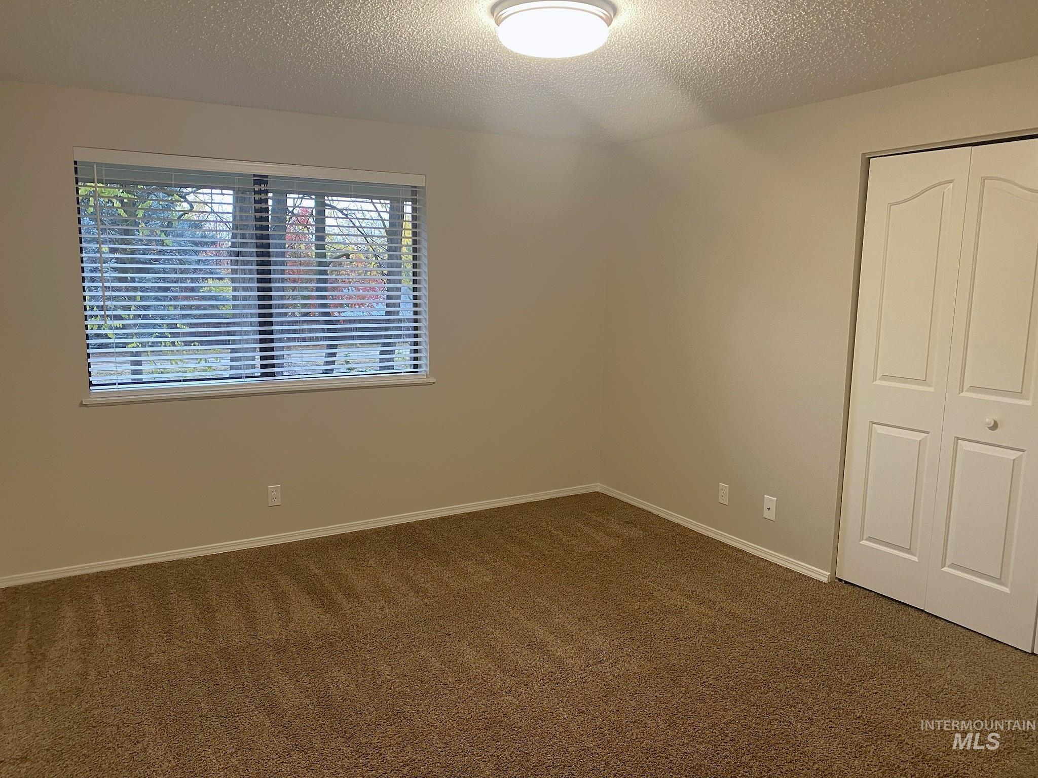 Unfurnished bedroom with dark colored carpet, a closet, and a textured ceiling