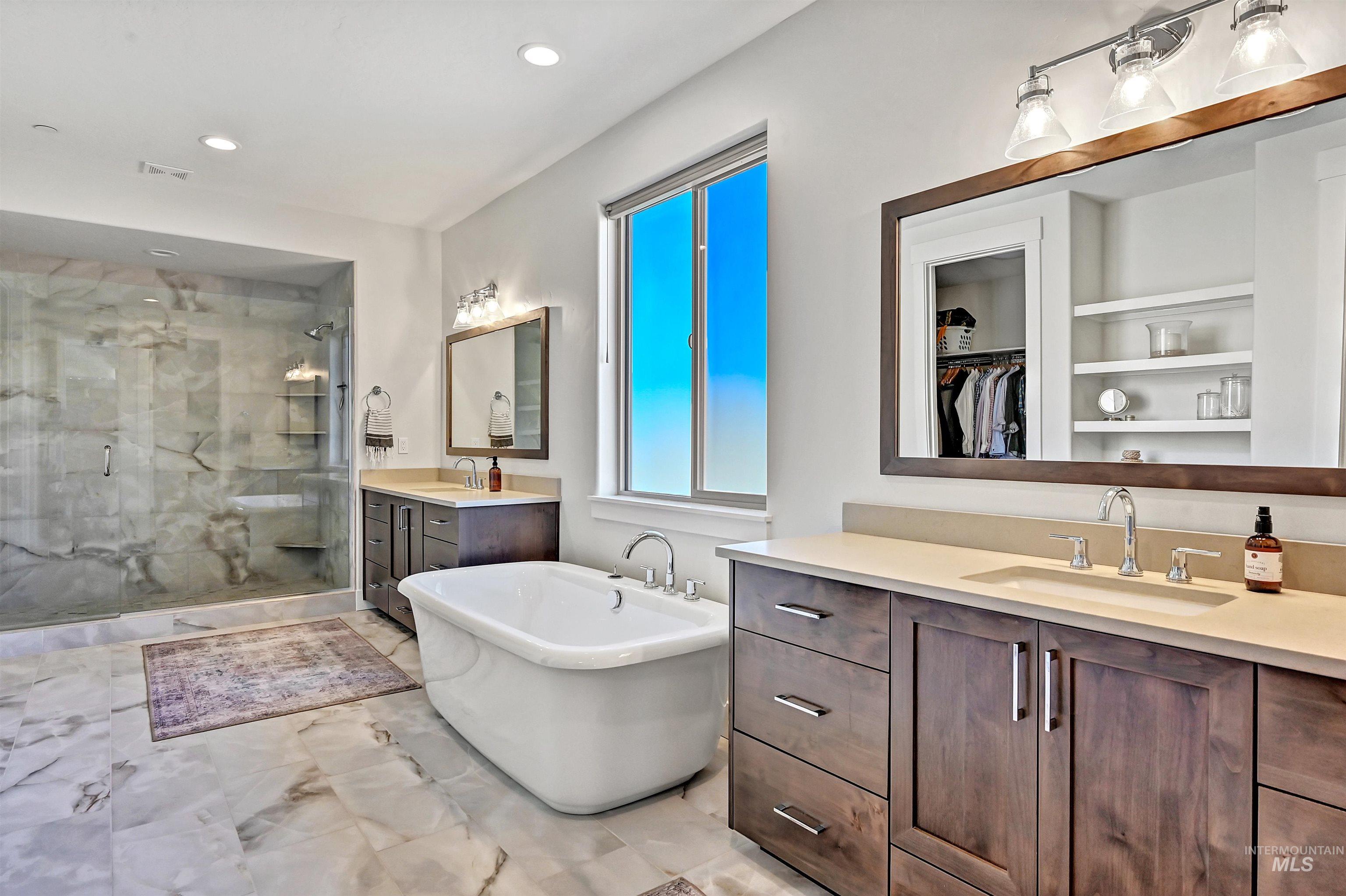Full bath with a shower stall, two vanities, a soaking tub, a spacious closet, and recessed lighting
