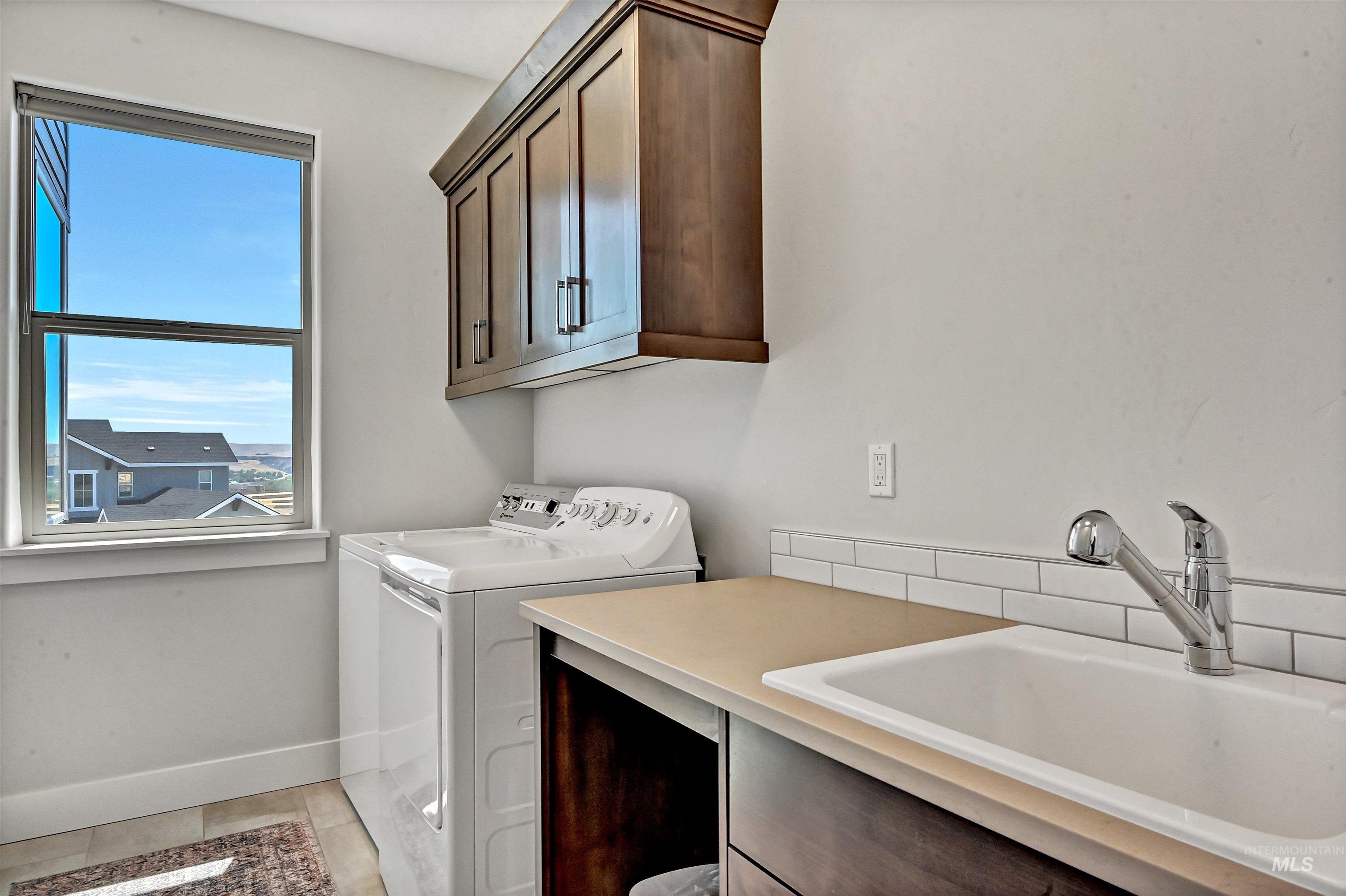 Laundry area featuring separate washer and dryer, light tile patterned flooring, and cabinet space