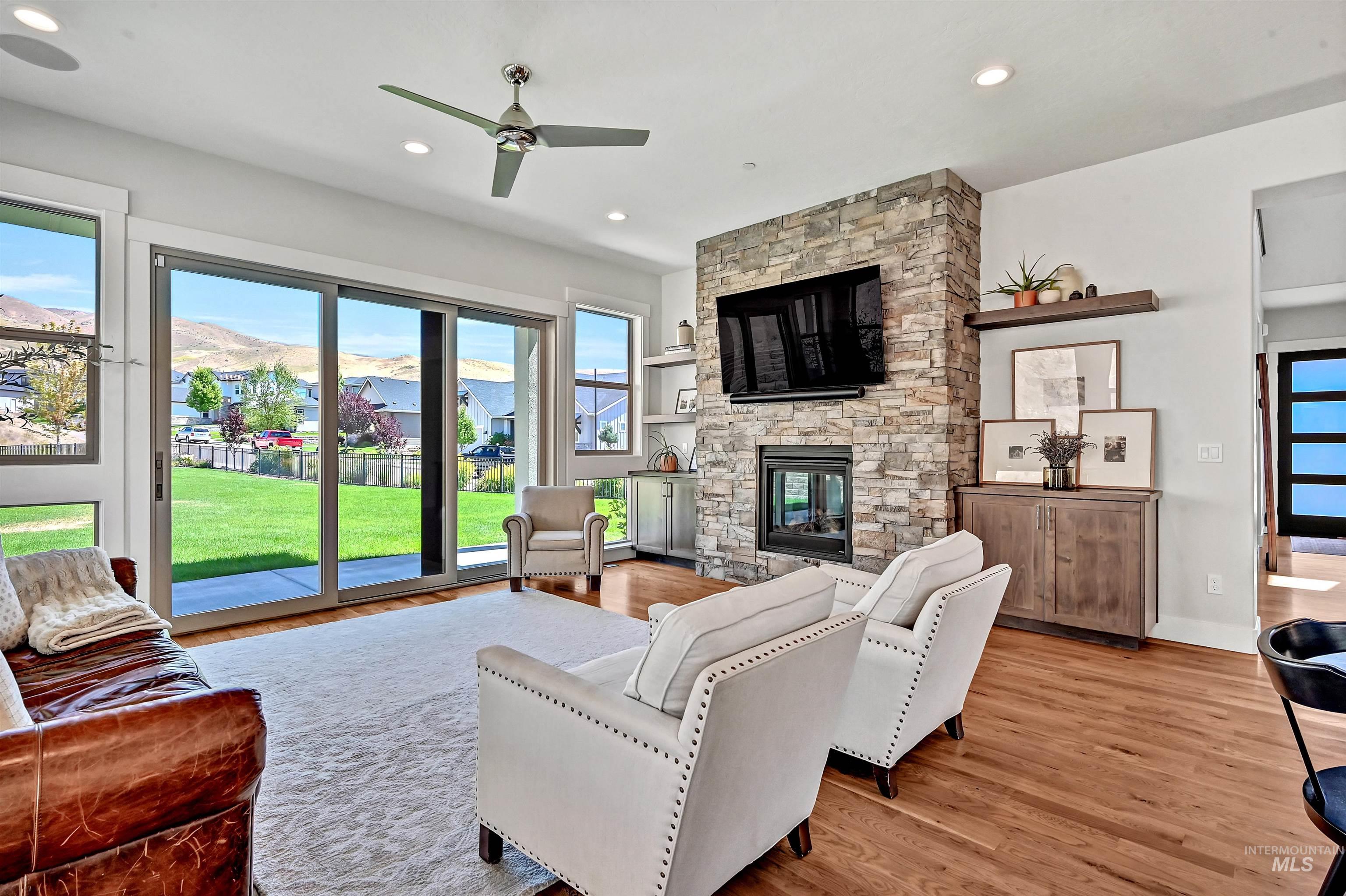 Living room with light wood finished floors, recessed lighting, a stone fireplace, and a ceiling fan