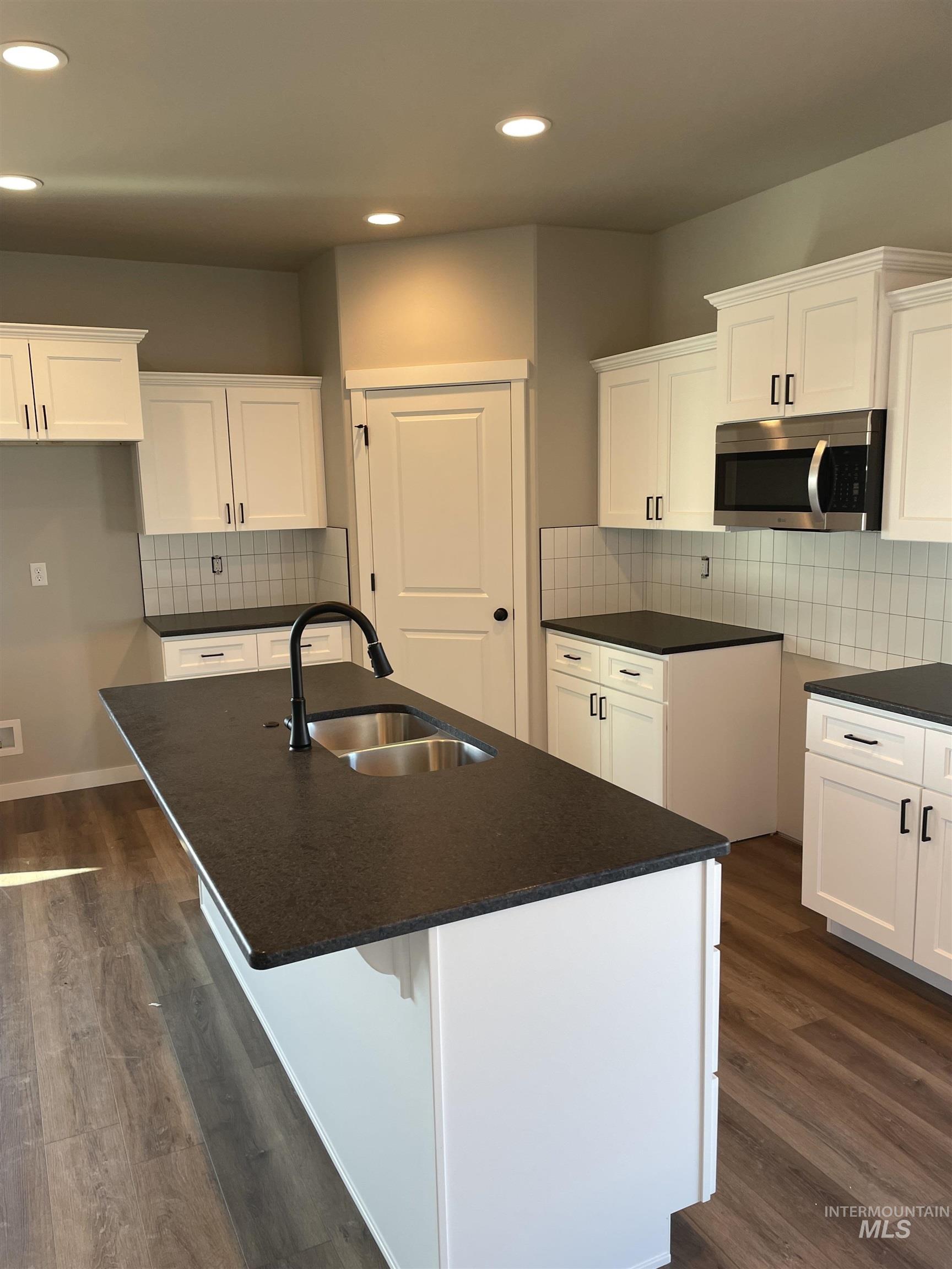 Kitchen with white cabinetry, backsplash, stainless steel microwave, recessed lighting, and dark wood-style flooring