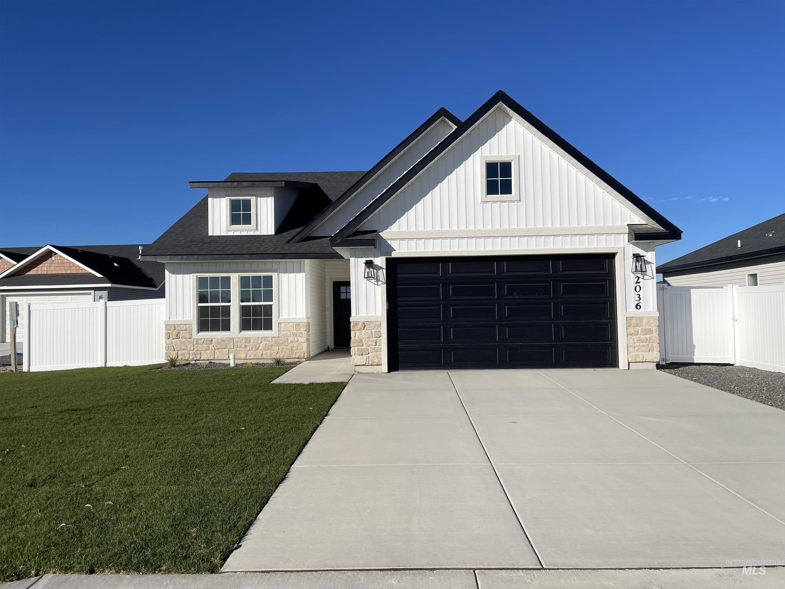 Modern inspired farmhouse featuring stone siding, a garage, driveway, and board and batten siding