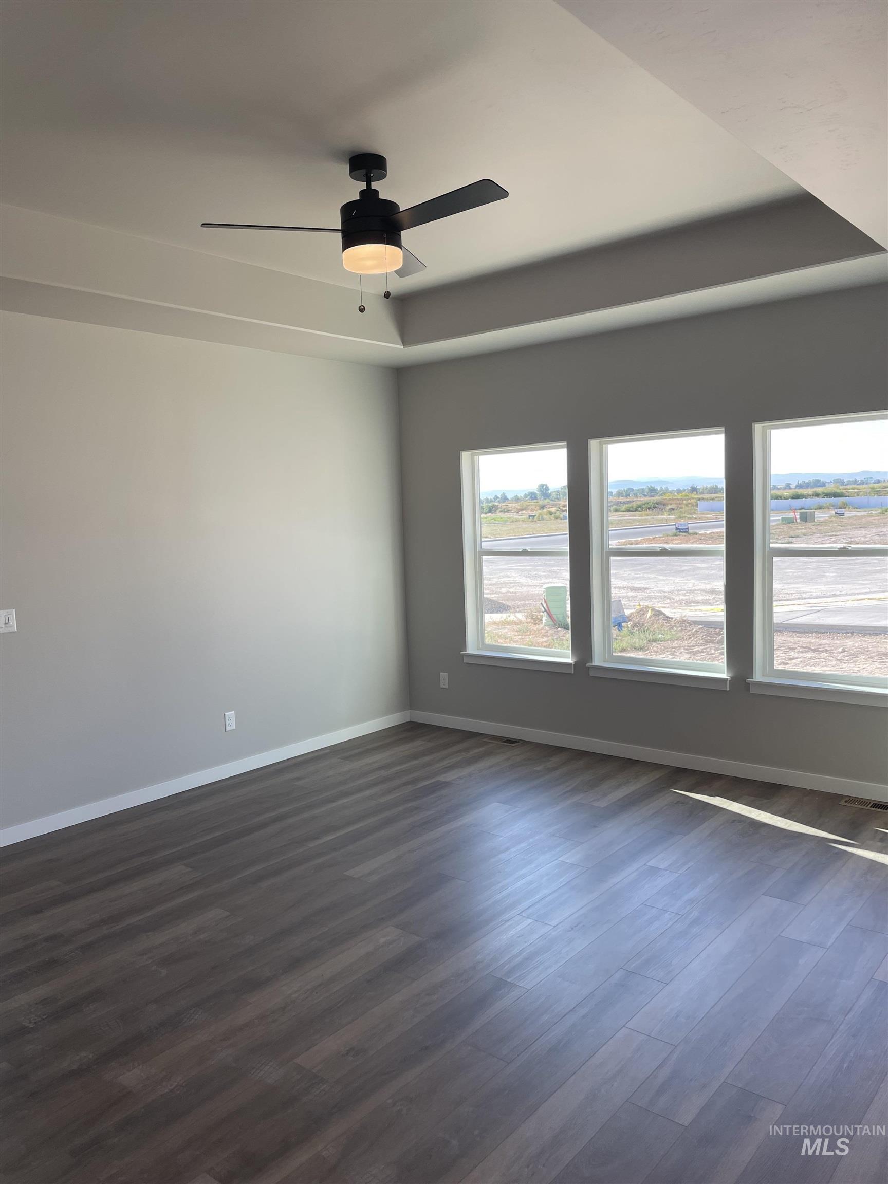 Unfurnished room with a tray ceiling, dark wood-style floors, and ceiling fan
