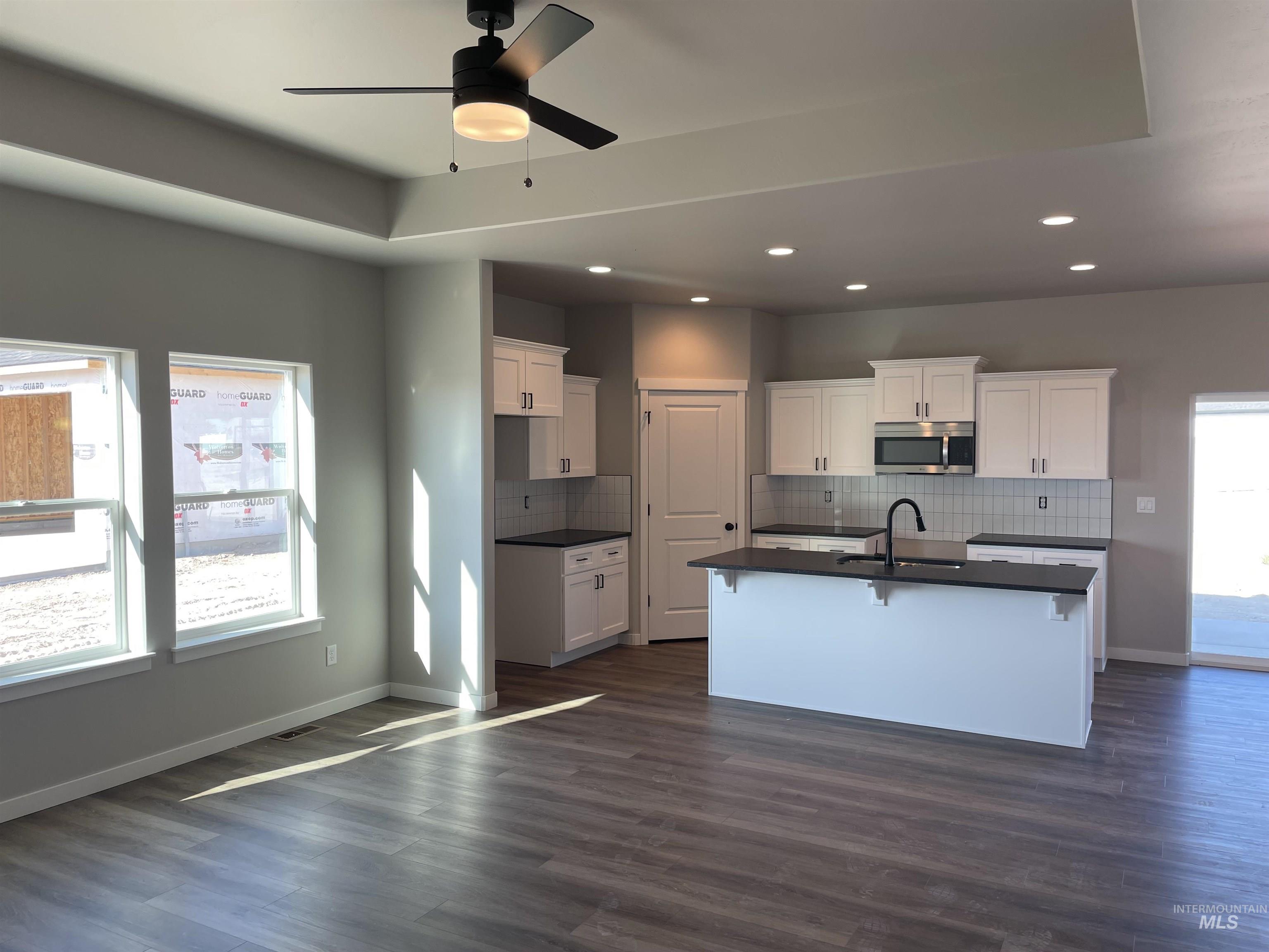 Kitchen with a kitchen bar, white cabinets, a kitchen island with sink, dark wood-style floors, and tasteful backsplash