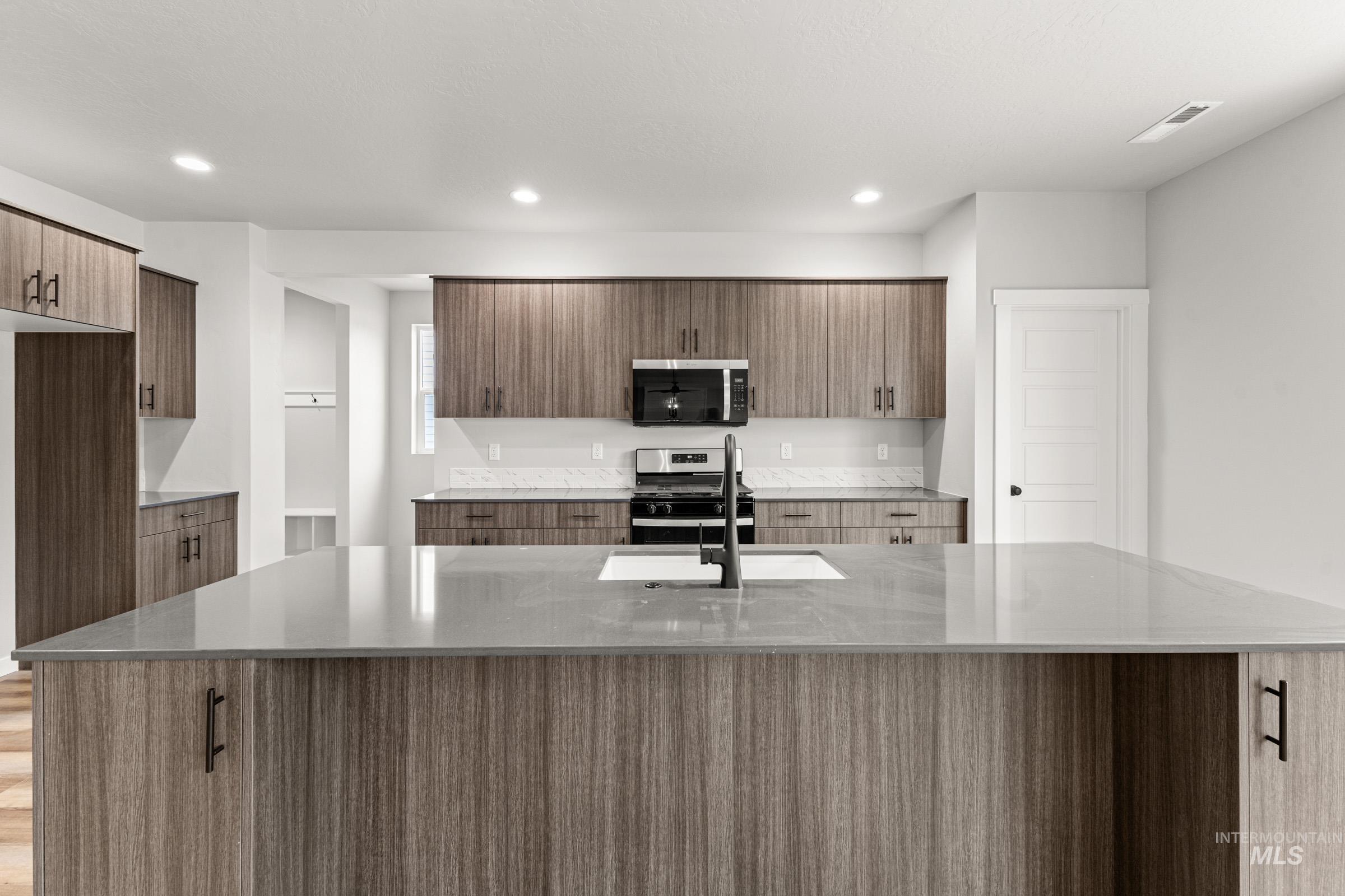 Kitchen with light stone counters, stainless steel appliances, a center island with sink, modern cabinets, and recessed lighting