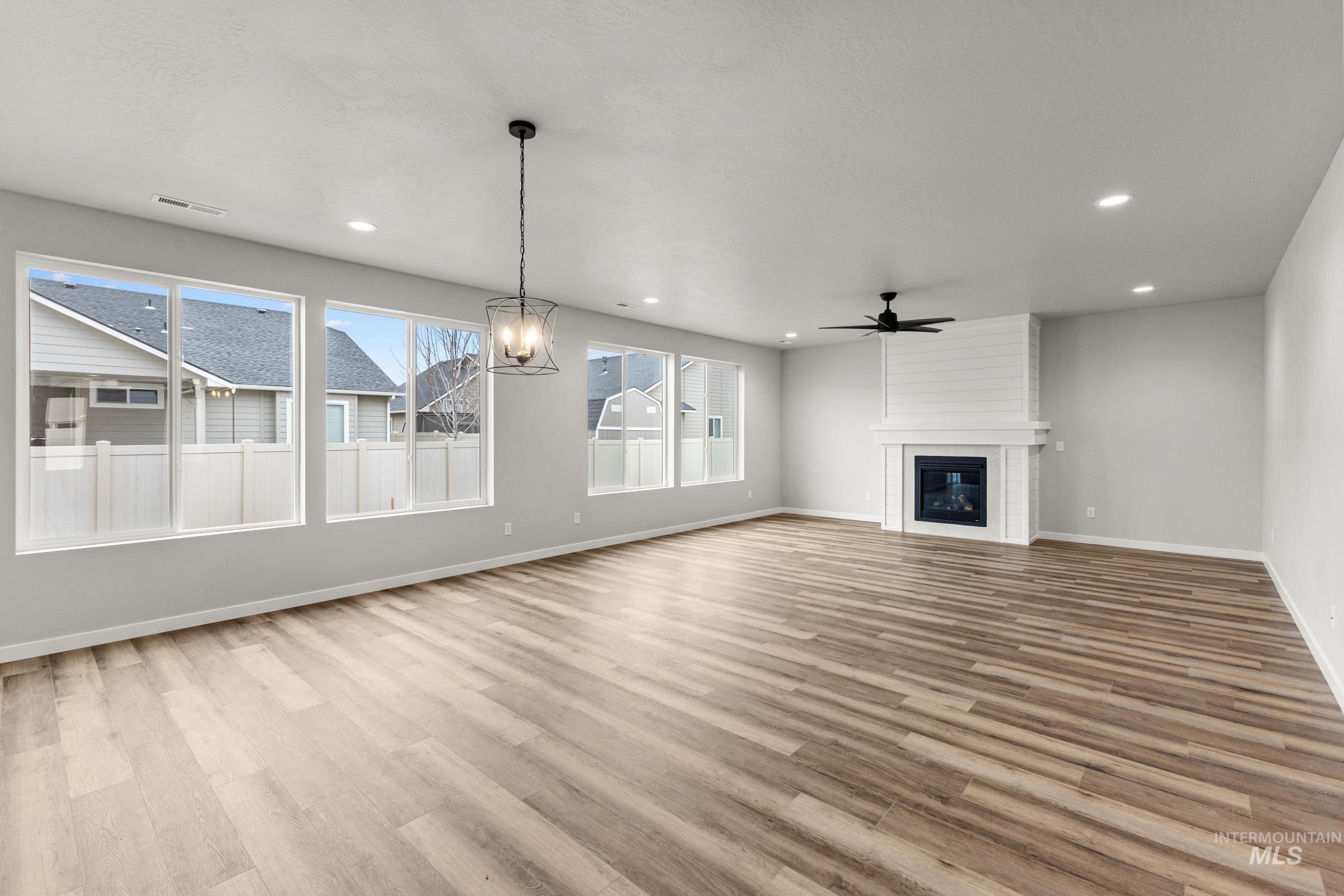 Unfurnished living room with a fireplace, light wood-type flooring, hanging lights, and a ceiling fan