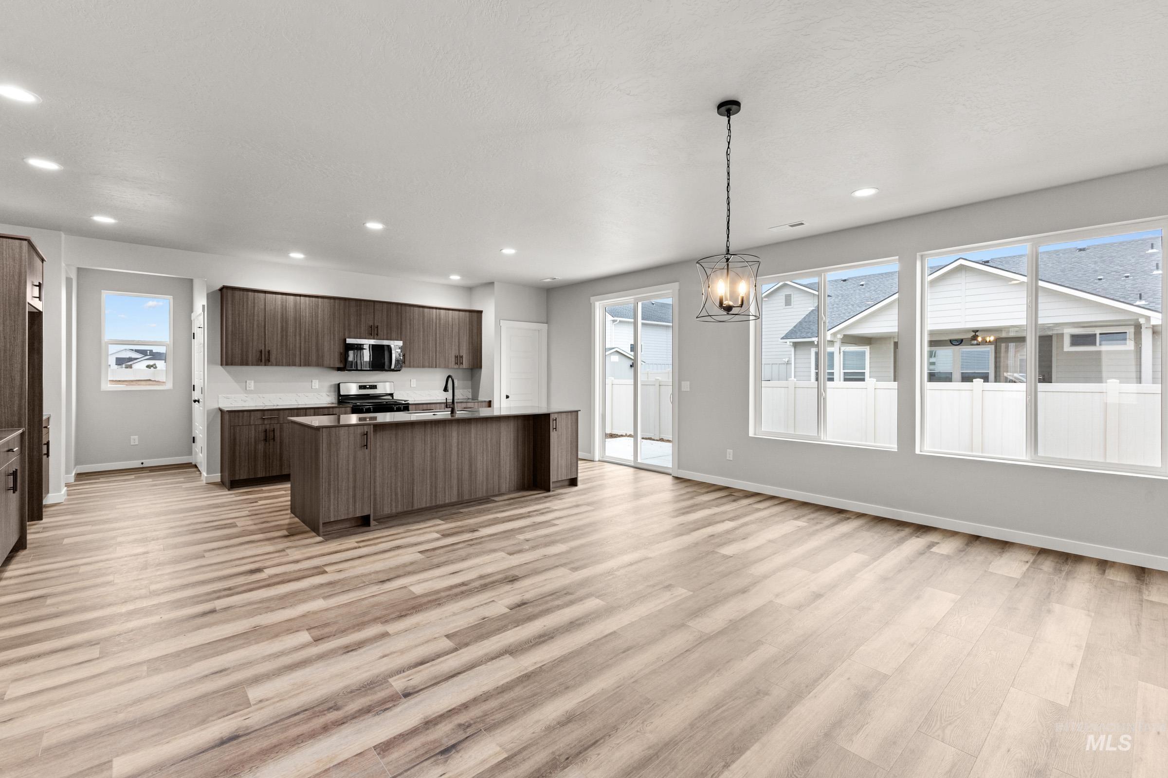 Kitchen with open floor plan, suspended lighting, stainless steel appliances, an island with sink, and light wood-type flooring