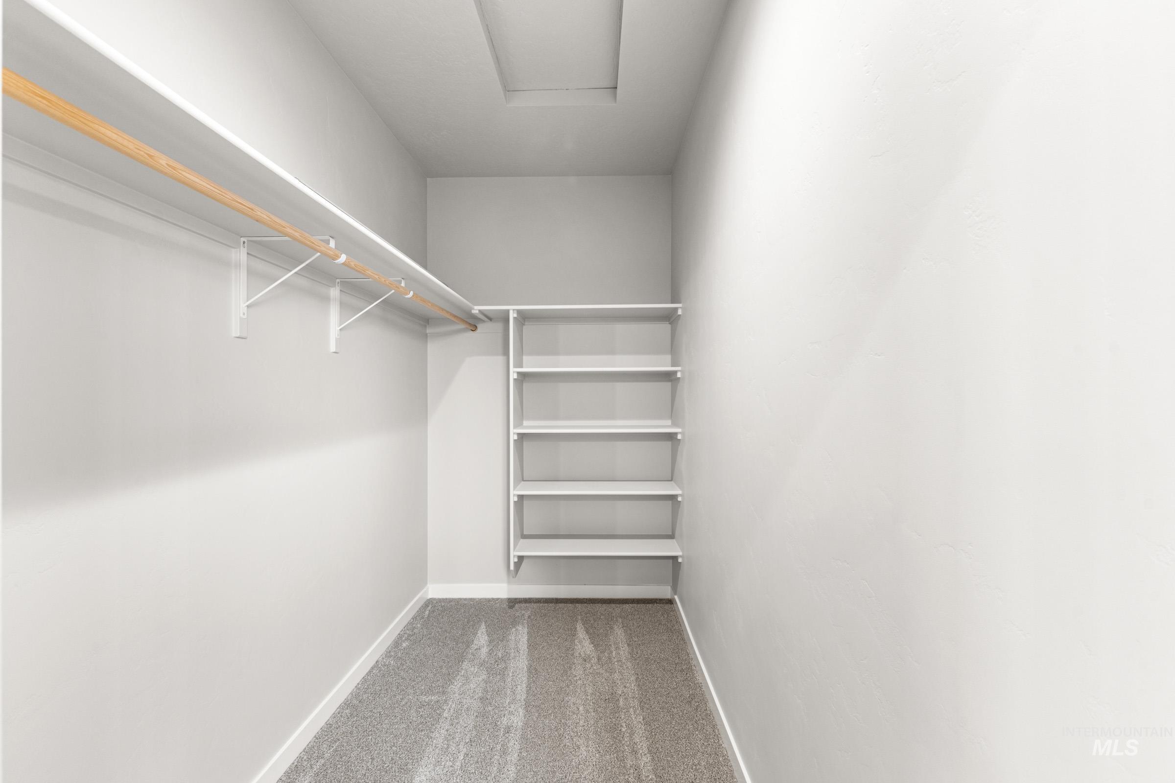 Walk in closet with light carpet and attic access