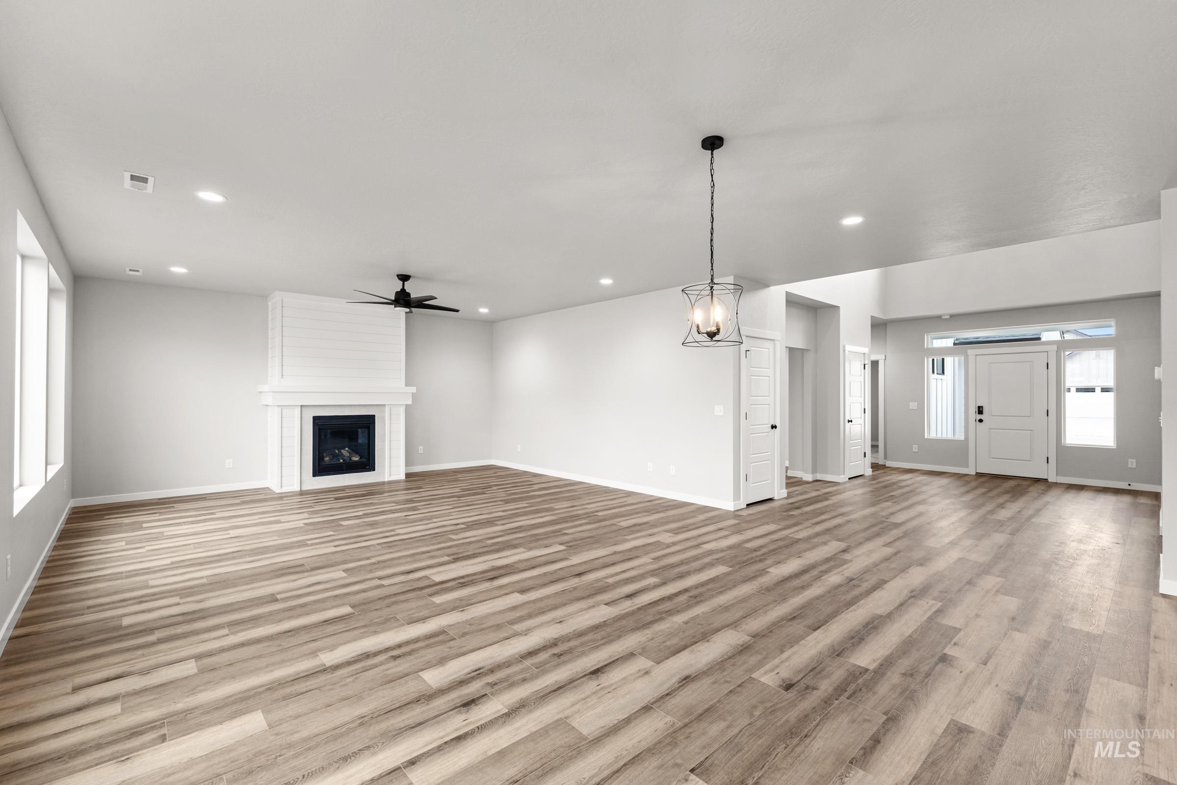 Unfurnished living room featuring a large fireplace, ceiling fan, light wood-style flooring, and a chandelier