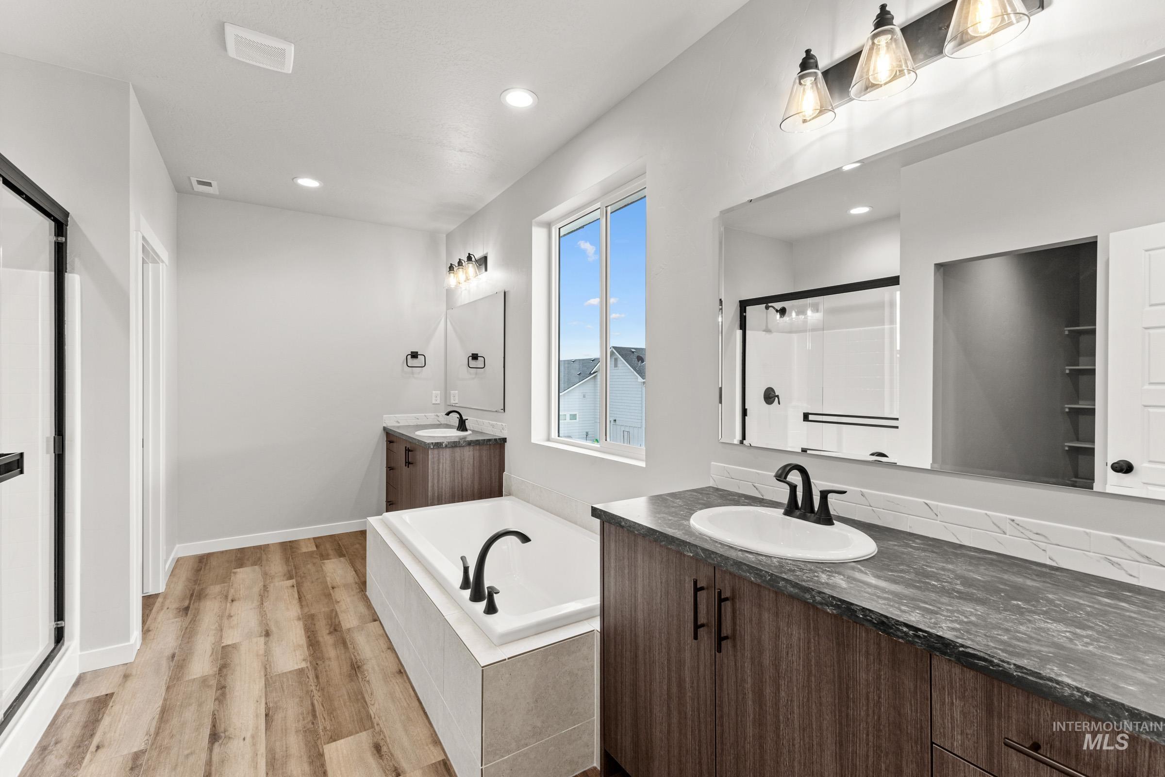 Bathroom featuring a stall shower, two vanities, a garden tub, light wood-style flooring, and recessed lighting