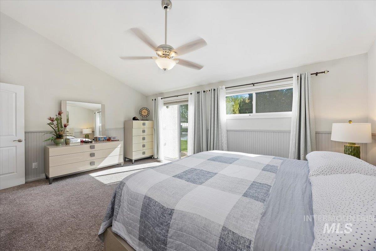 Bedroom with a wainscoted wall, carpet flooring, access to outside, a ceiling fan, and vaulted ceiling