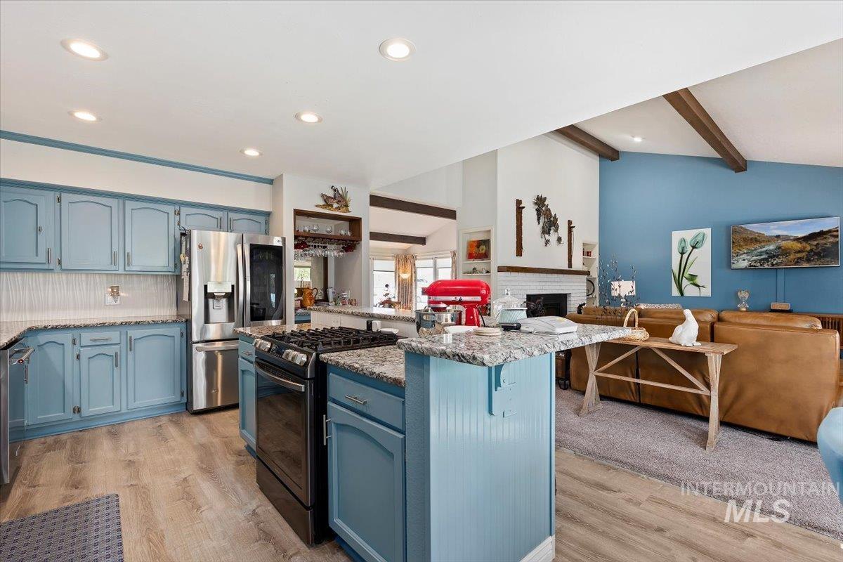 Kitchen featuring blue cabinets, stainless steel appliances, light stone counters, open floor plan, and recessed lighting