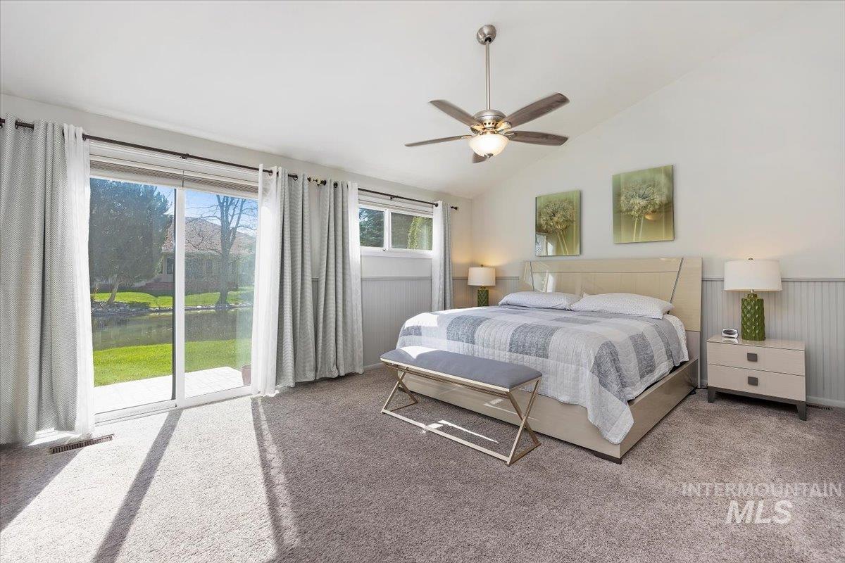 Carpeted bedroom with access to outside, lofted ceiling, a ceiling fan, wainscoting, and a water view