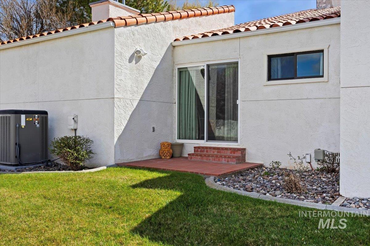 Back of property with a yard, a tiled roof, entry steps, and stucco siding