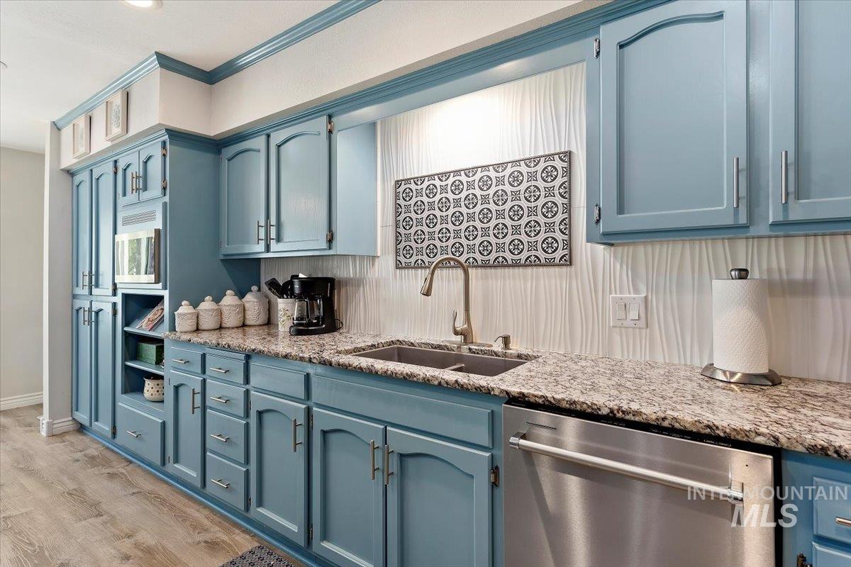 Kitchen featuring blue cabinetry, stainless steel appliances, light stone counters, light wood finished floors, and tasteful backsplash