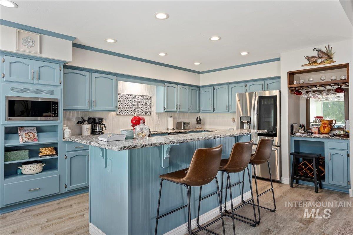 Kitchen featuring blue cabinets, stainless steel appliances, light wood finished floors, light stone countertops, and recessed lighting