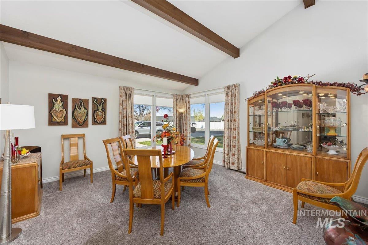 Carpeted dining room featuring vaulted ceiling with beams and baseboards