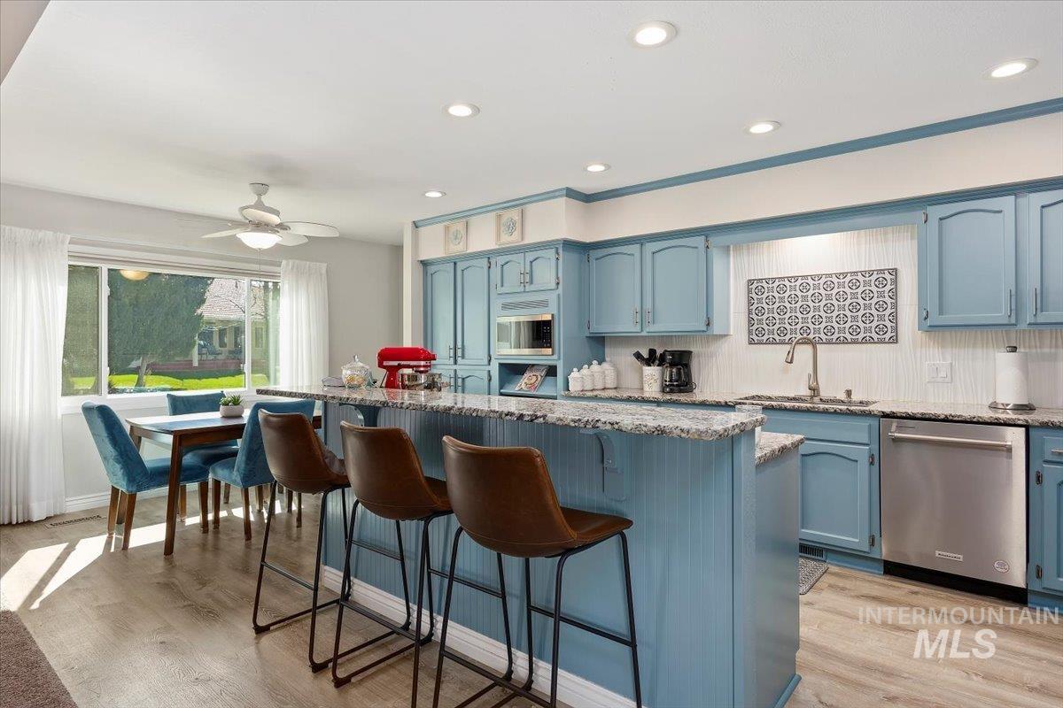 Kitchen featuring blue cabinets, light stone counters, stainless steel appliances, light wood finished floors, and ceiling fan