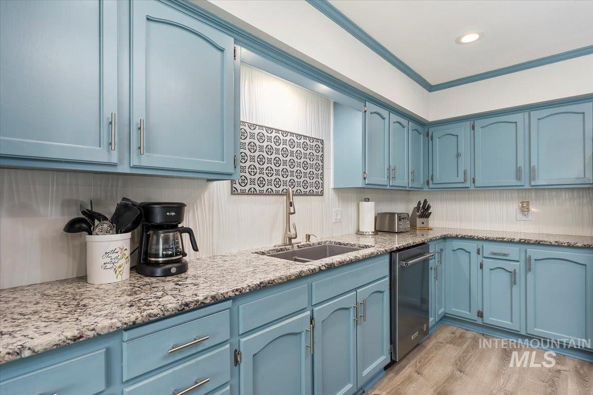 Kitchen with blue cabinetry, light stone countertops, light wood finished floors, crown molding, and stainless steel dishwasher