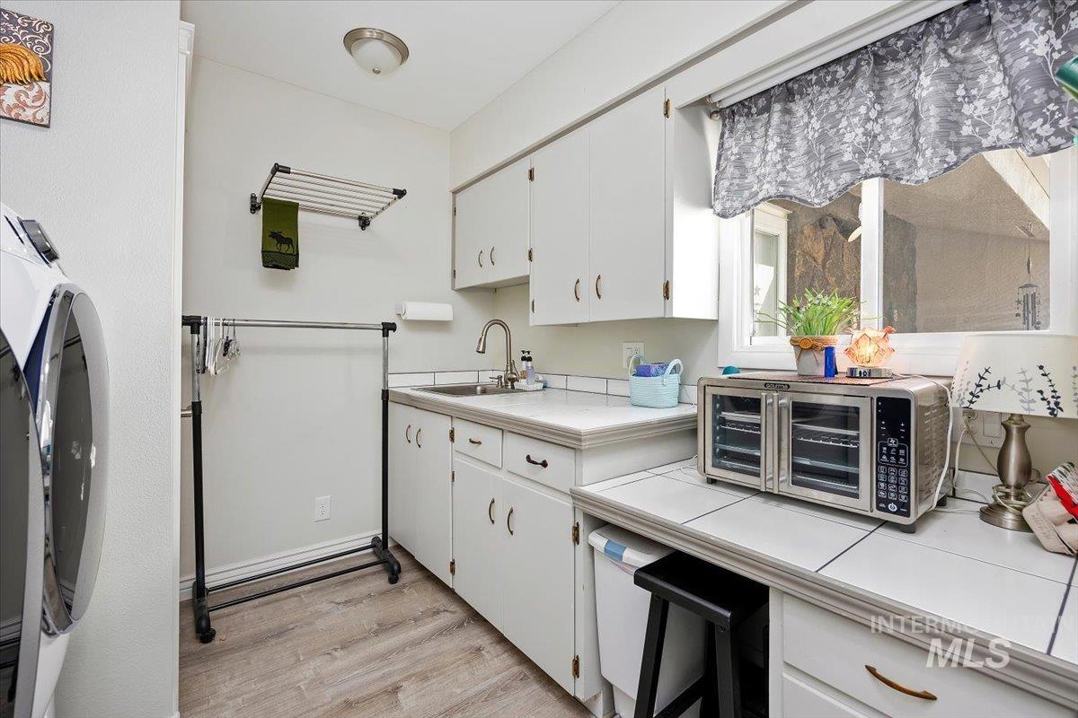 Kitchen featuring white cabinets, tile counters, and light wood-style floors