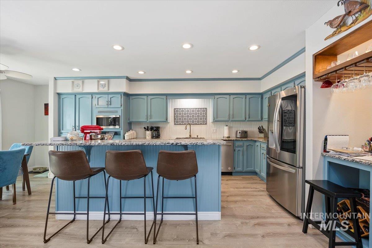 Kitchen featuring a kitchen bar, light stone counters, decorative backsplash, stainless steel appliances, and blue cabinetry