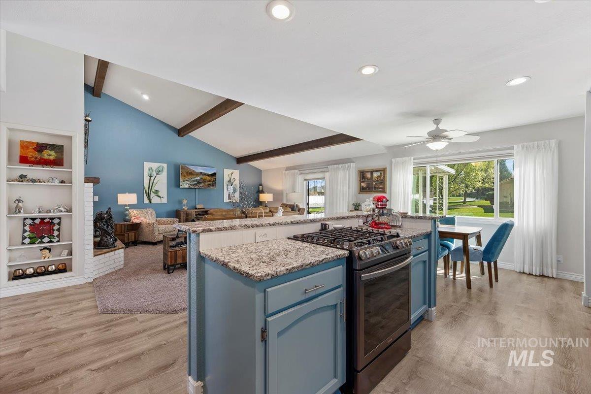 Kitchen featuring blue cabinetry, stainless steel gas range, light stone counters, open floor plan, and a kitchen island