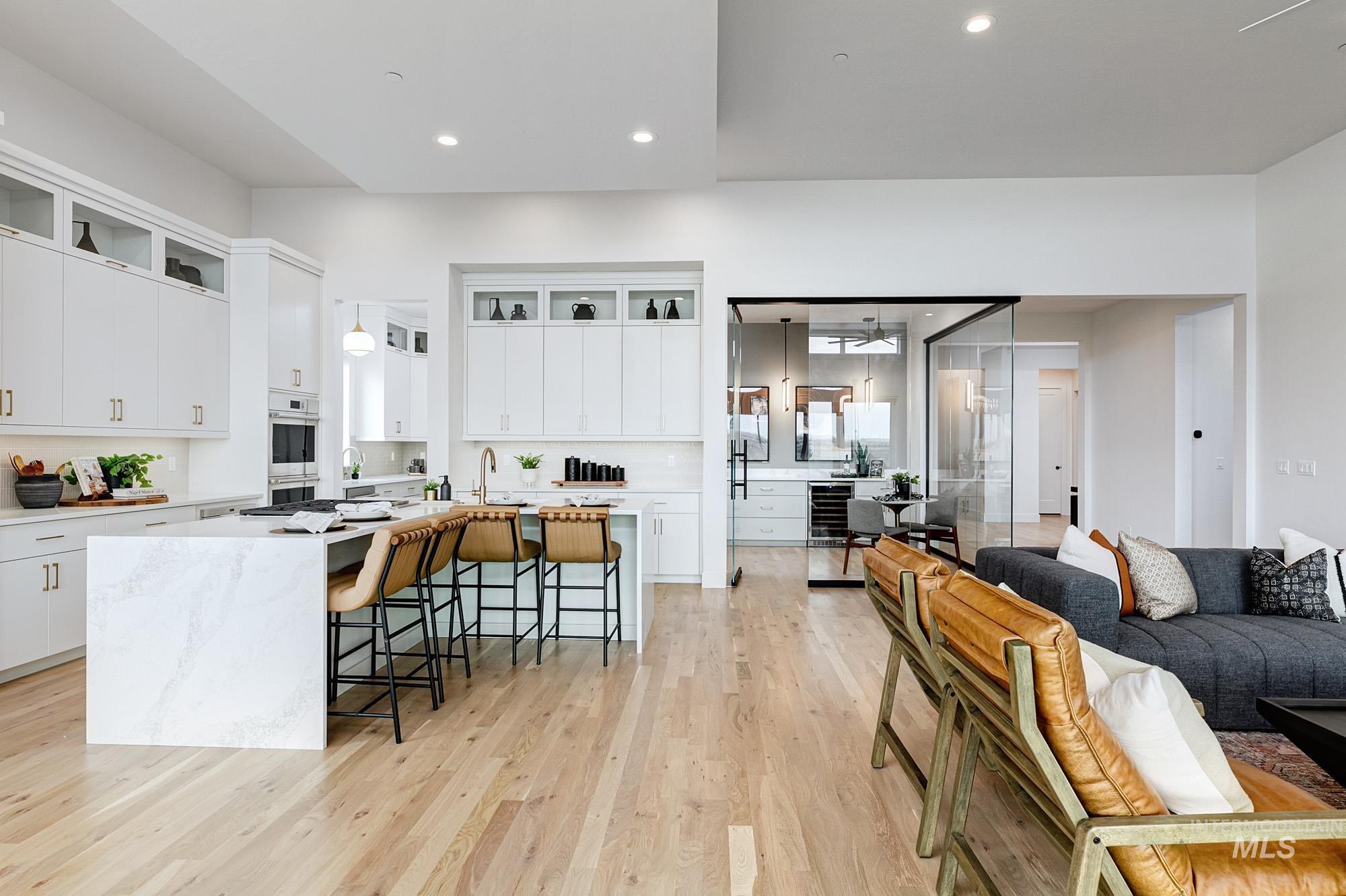 Gourmet kitchen featuring a waterfall island with integrated seating, white cabinetry with gold-finish hardware, built-in double ovens, and a dedicated beverage refrigerator area