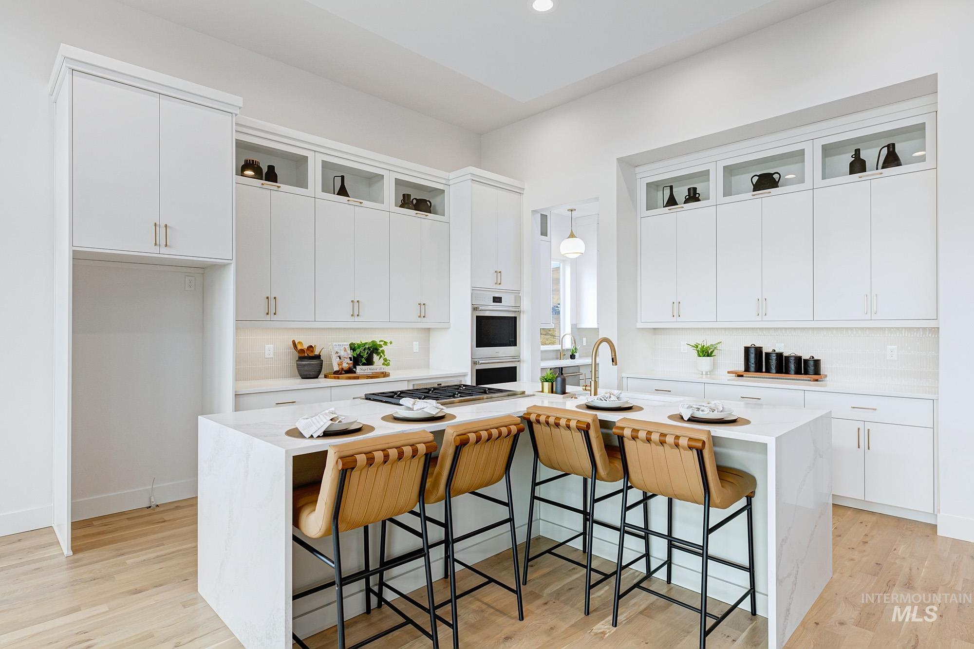Gourmet kitchen featuring a waterfall island with integrated seating, extensive white cabinetry with gold-finish hardware, built-in oven and microwave, and a gold-finish gooseneck faucet