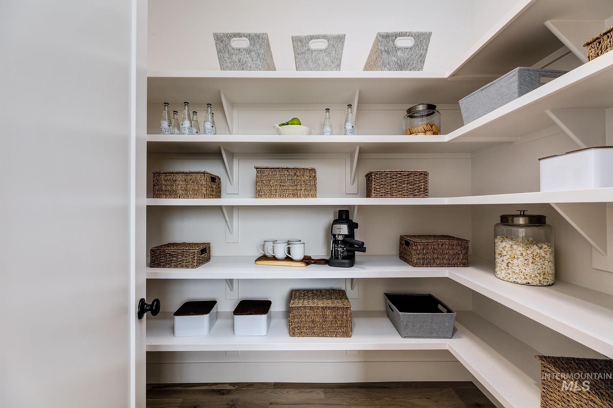 Corner pantry featuring extensive white shelving, wood-finish flooring, and a black doorknob